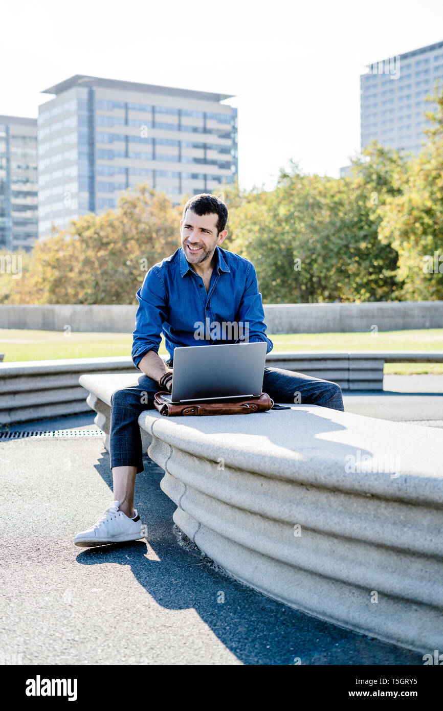 Portrait of smiling businessman sitting on bench outdoors working on laptop Banque D'Images