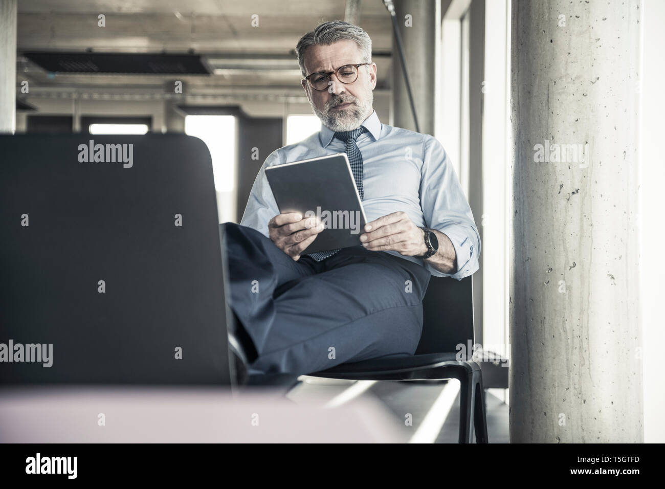 Mature businessman sitting on chair à l'aide de tablet Banque D'Images
