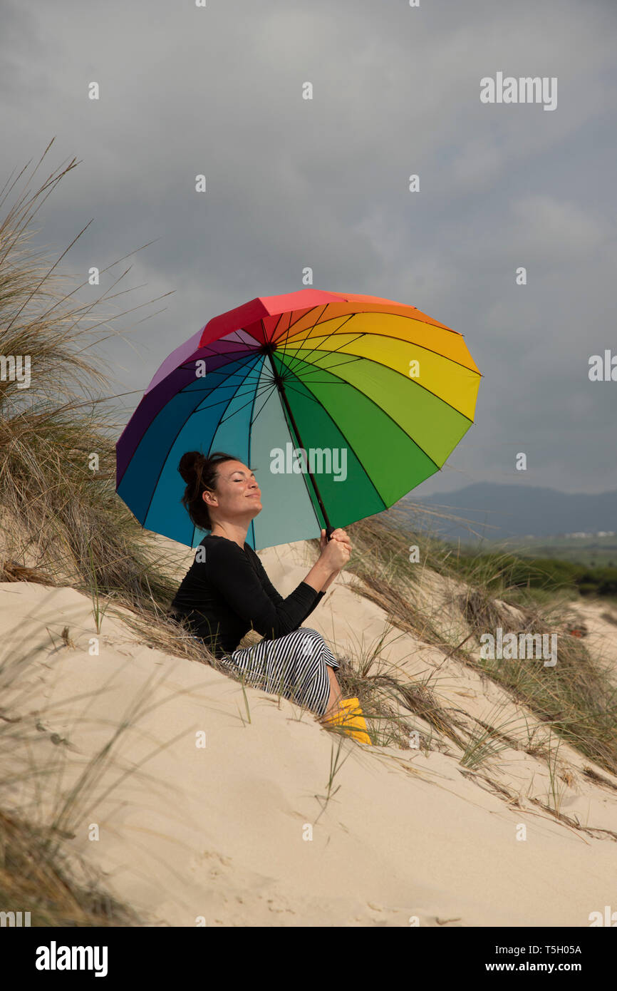 Femme avec parapluie coloré assis sur la plage, les bains de soleil Banque D'Images