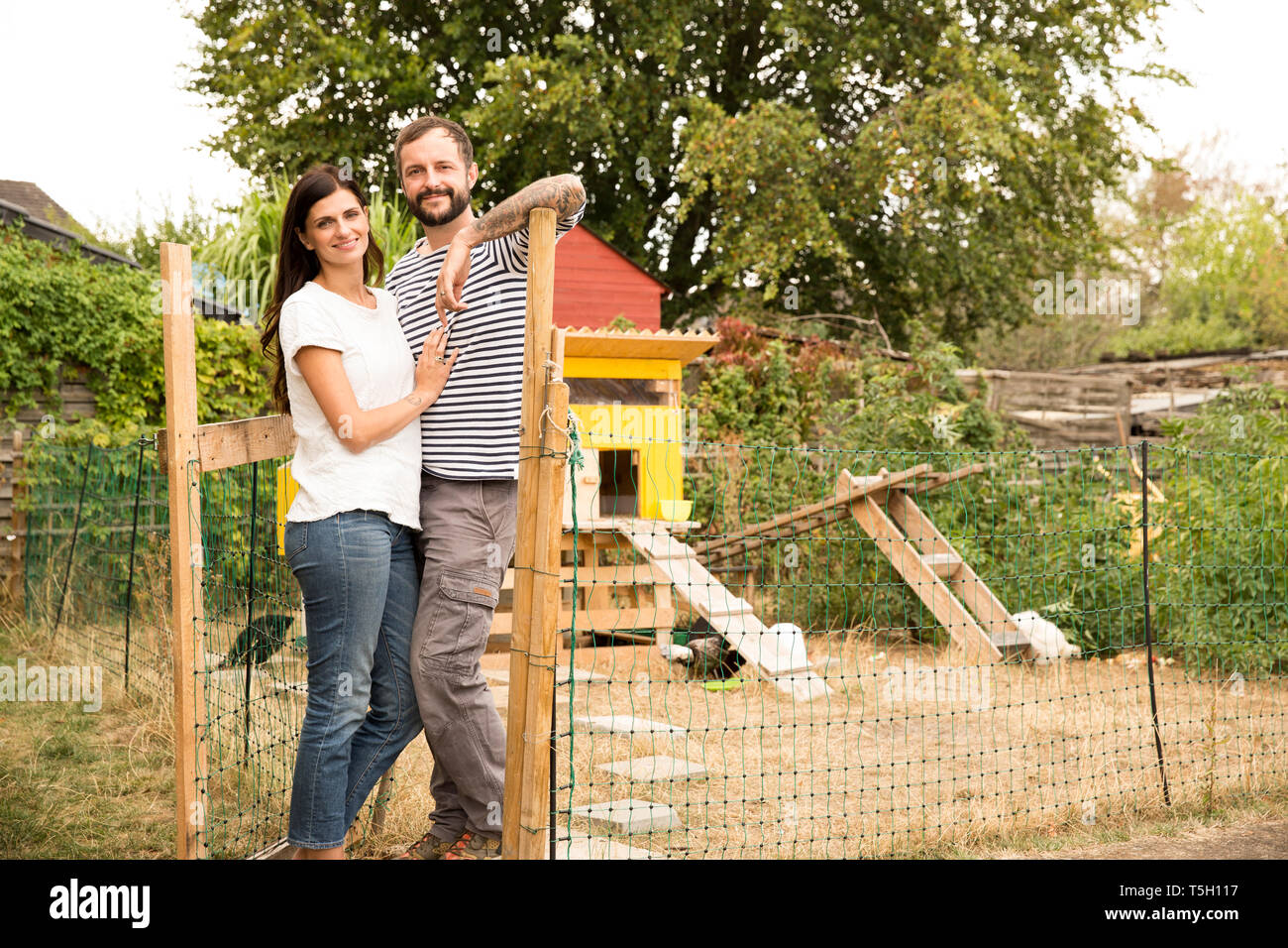 Portrait of smiling couple standing à chickenhouse in garden Banque D'Images