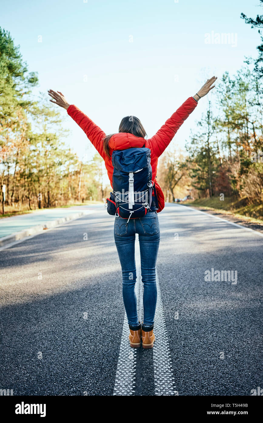 Happy woman raising arms au milieu d'une route vide lors de randonnée Banque D'Images