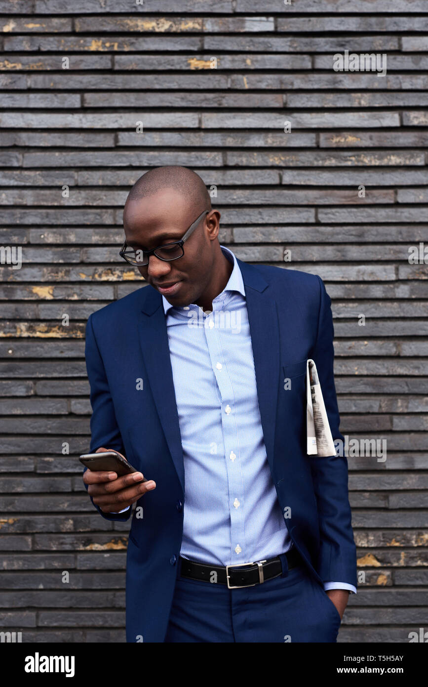 Portrait of smiling businessman with newspaper portant des lunettes et costume bleu looking at mobile phone Banque D'Images