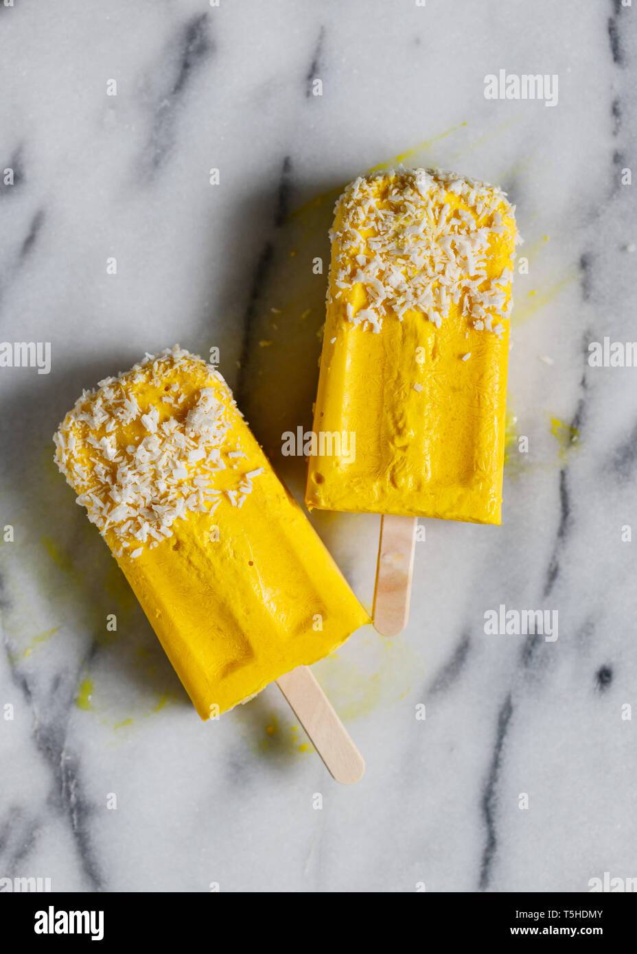 Vue du dessus des deux sucettes glacées sont fabriqués à partir de lait de coco et de mangue surgelés plus de marbre blanc. La nourriture végétalienne saine et à l'été. Banque D'Images