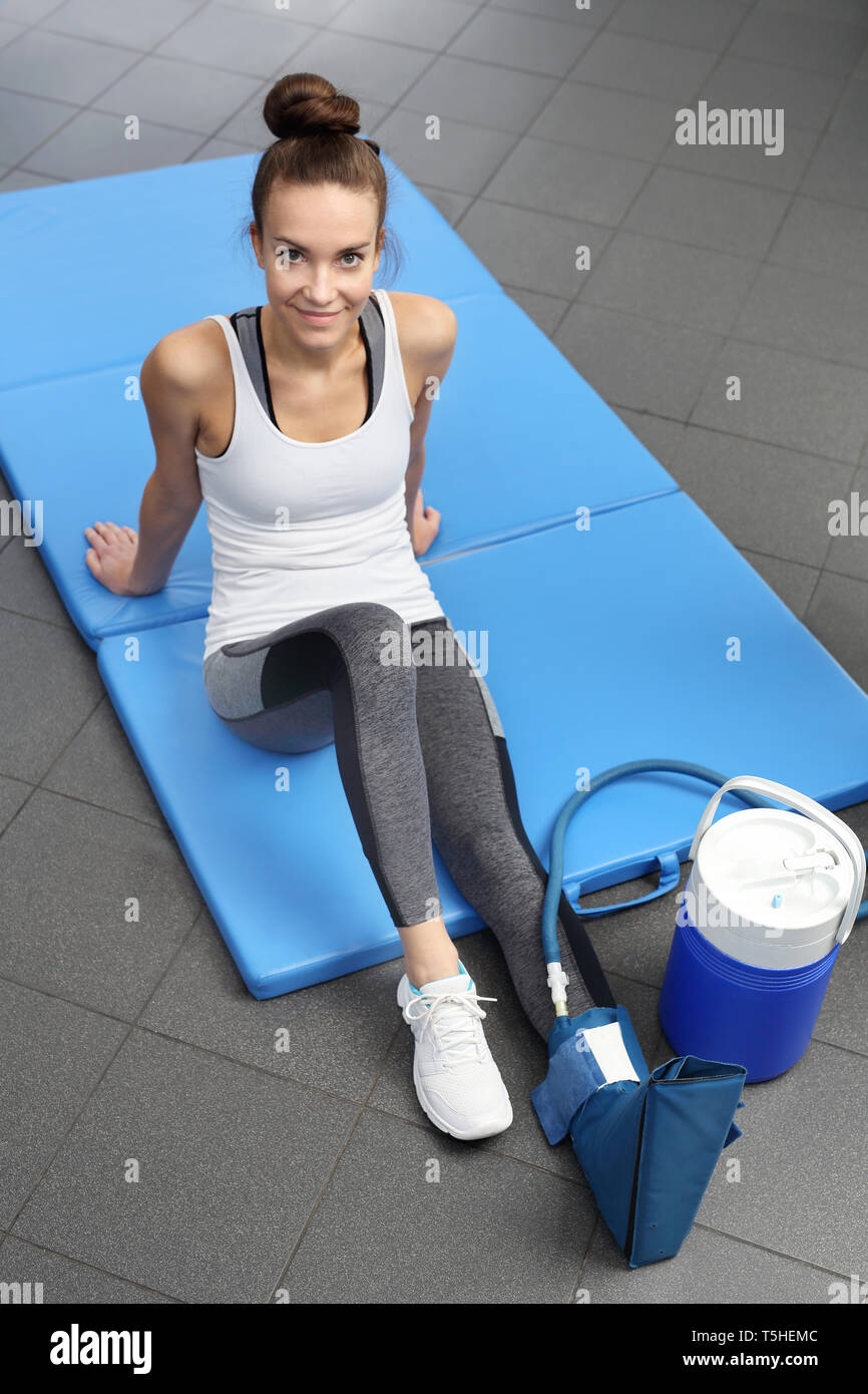 Une femme avec une compresse de refroidissement sur sa jambe est assis sur un matelas dans une clinique de réadaptation. Banque D'Images