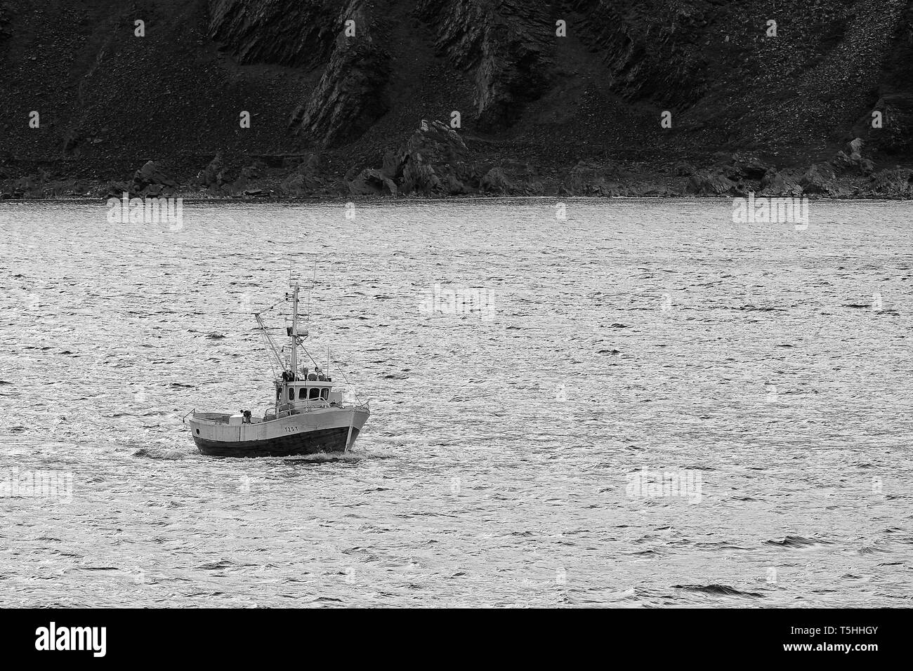 Photo en noir et blanc d'Un petit bateau de pêche commercial norvégien en route, À quelques kilomètres à l'ouest de Honningsvåg, au-dessus du cercle polaire arctique en Norvège. Banque D'Images