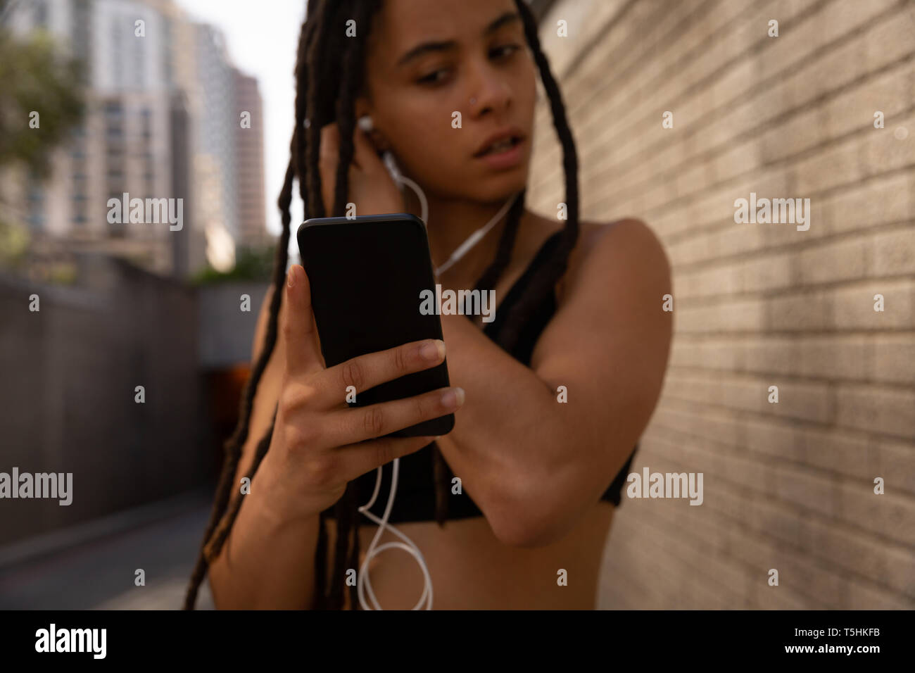 Young woman wearing earphones lors de l'utilisation de téléphone mobile dans la rue Banque D'Images