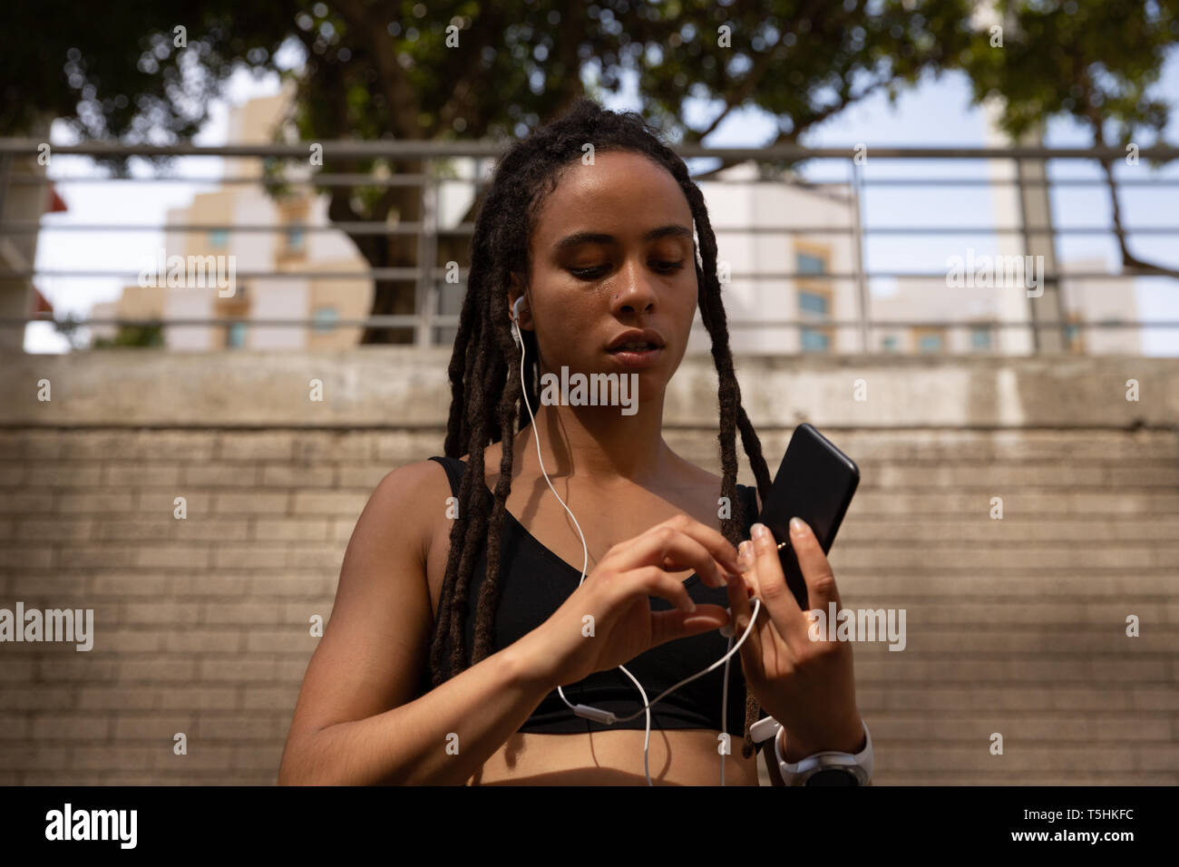 Young woman wearing earphones lors de l'utilisation de téléphone mobile dans la rue Banque D'Images