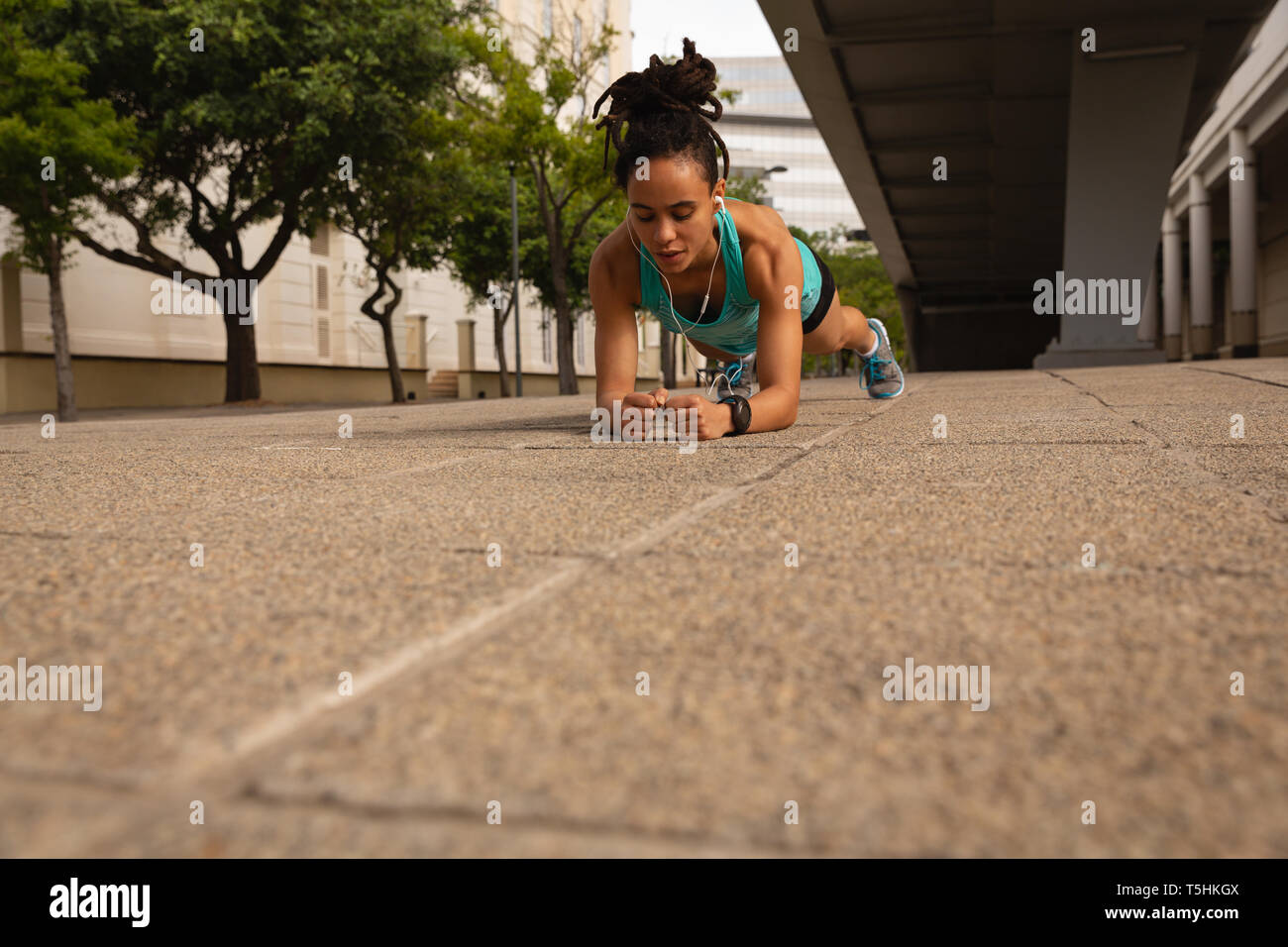 Woman listening music écouteurs sur planche tout en faisant de l'exercice dans la ville Banque D'Images Woman listening music écouteurs sur planche tout en faisant de l'exercice dans la ville Banque D'Images