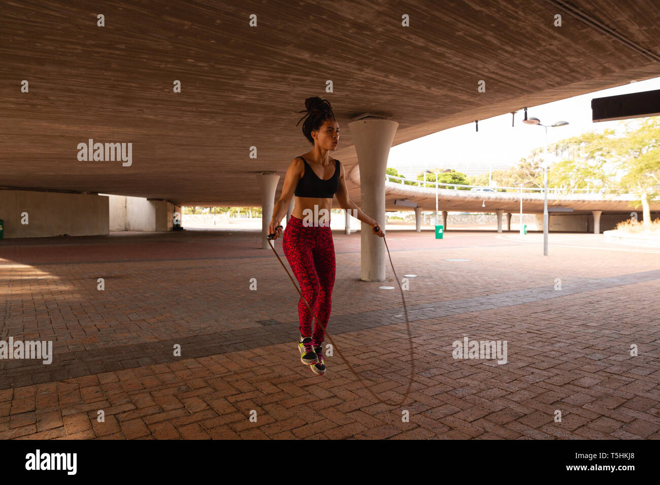 Young woman exercising with la corde à sauter sous un pont Banque D'Images Young woman exercising with la corde à sauter sous un pont Banque D'Images