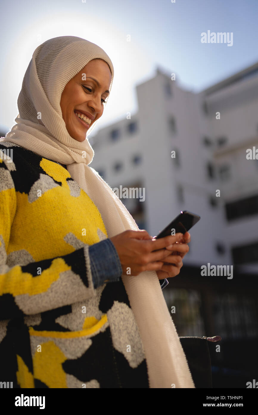 Woman using mobile phone en marchant dans la rue sur une journée ensoleillée Banque D'Images Woman using mobile phone en marchant dans la rue sur une journée ensoleillée Banque D'Images
