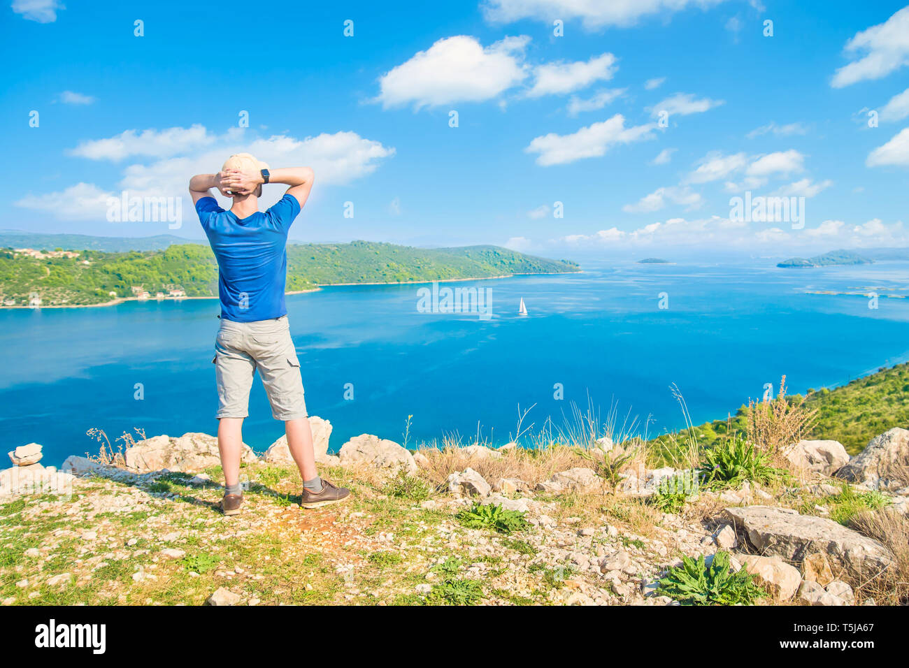 Young caucasian man standing at cliff en regardant sur la mer et les îles aux beaux jours de l'été, l'île de Rab, Croatie Banque D'Images