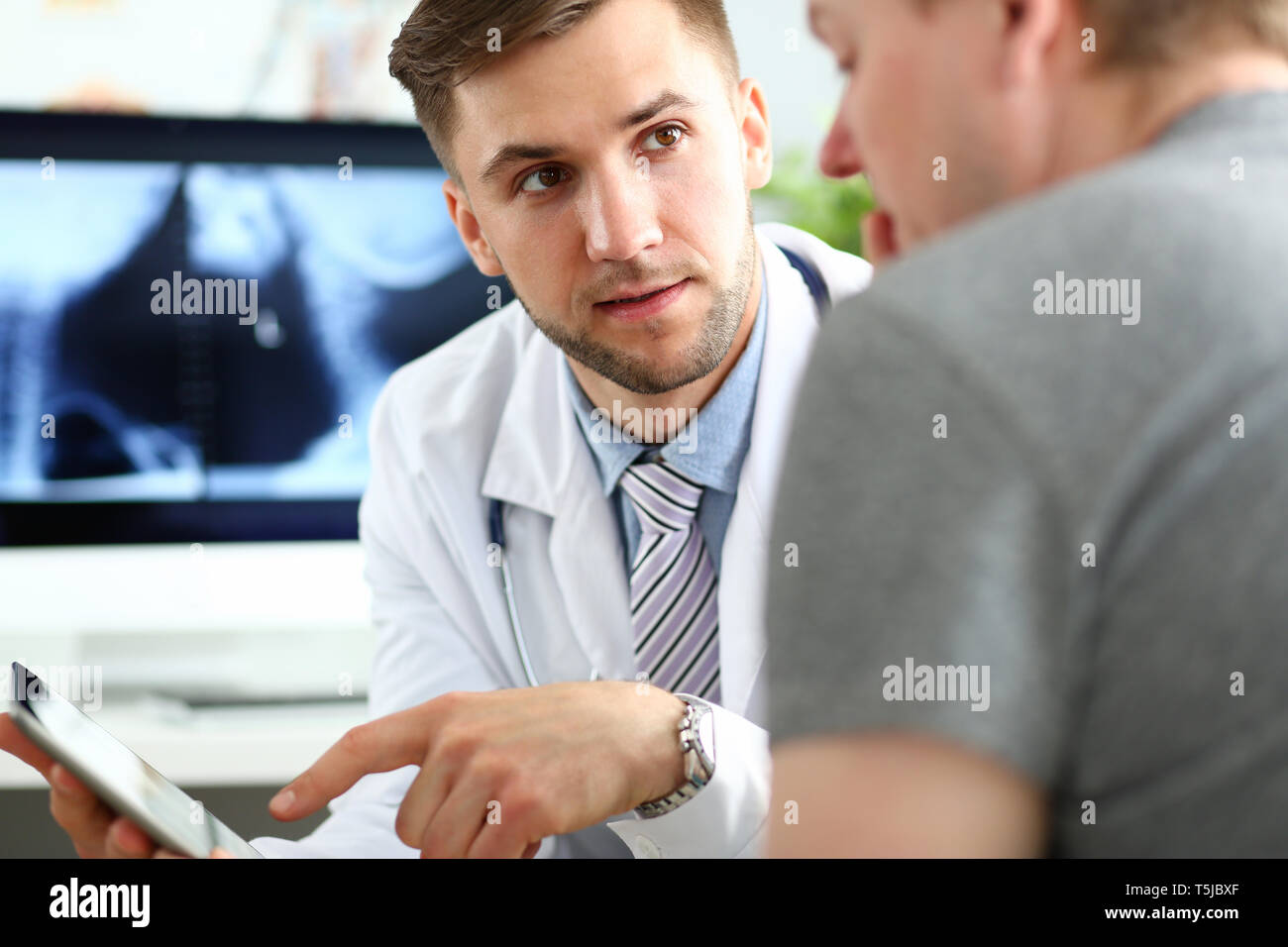 Beau mâle médecin patient consultation montrant quelque chose à l'écran du PC tablette Banque D'Images