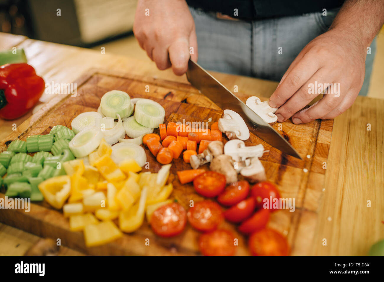 Chef de la main d'entaille les champignons sur planche en bois libre. Homme couper des légumes sur le comptoir de cuisine, une salade fraîche, cuisine intérieur sur arrière-plan. Banque D'Images