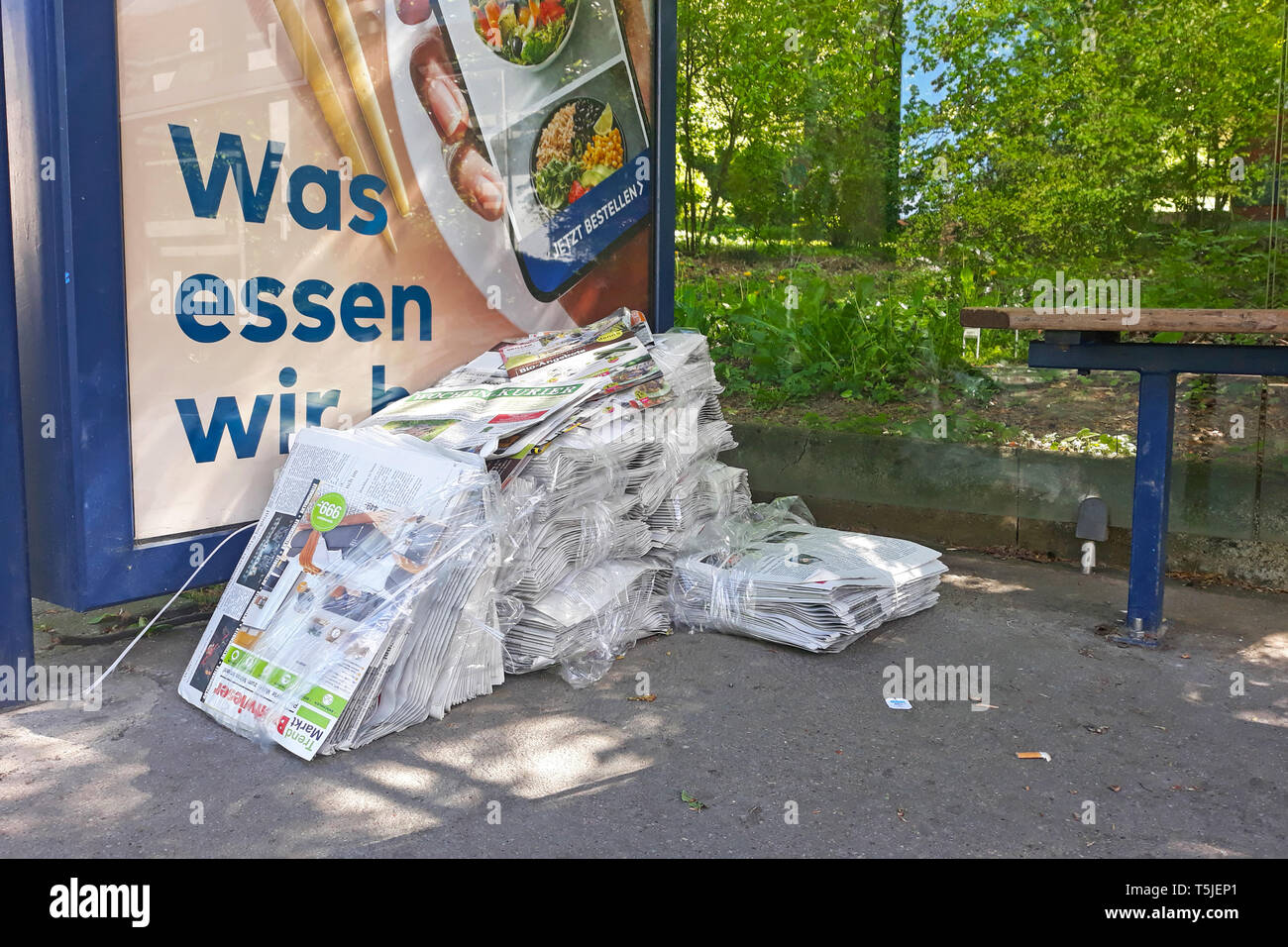 Pile de journal local gratuit des marchandises sous-évaluées à un arrêt de bus par courier paresseux qui était payé pour les livrer à des boîtes aux lettres Banque D'Images