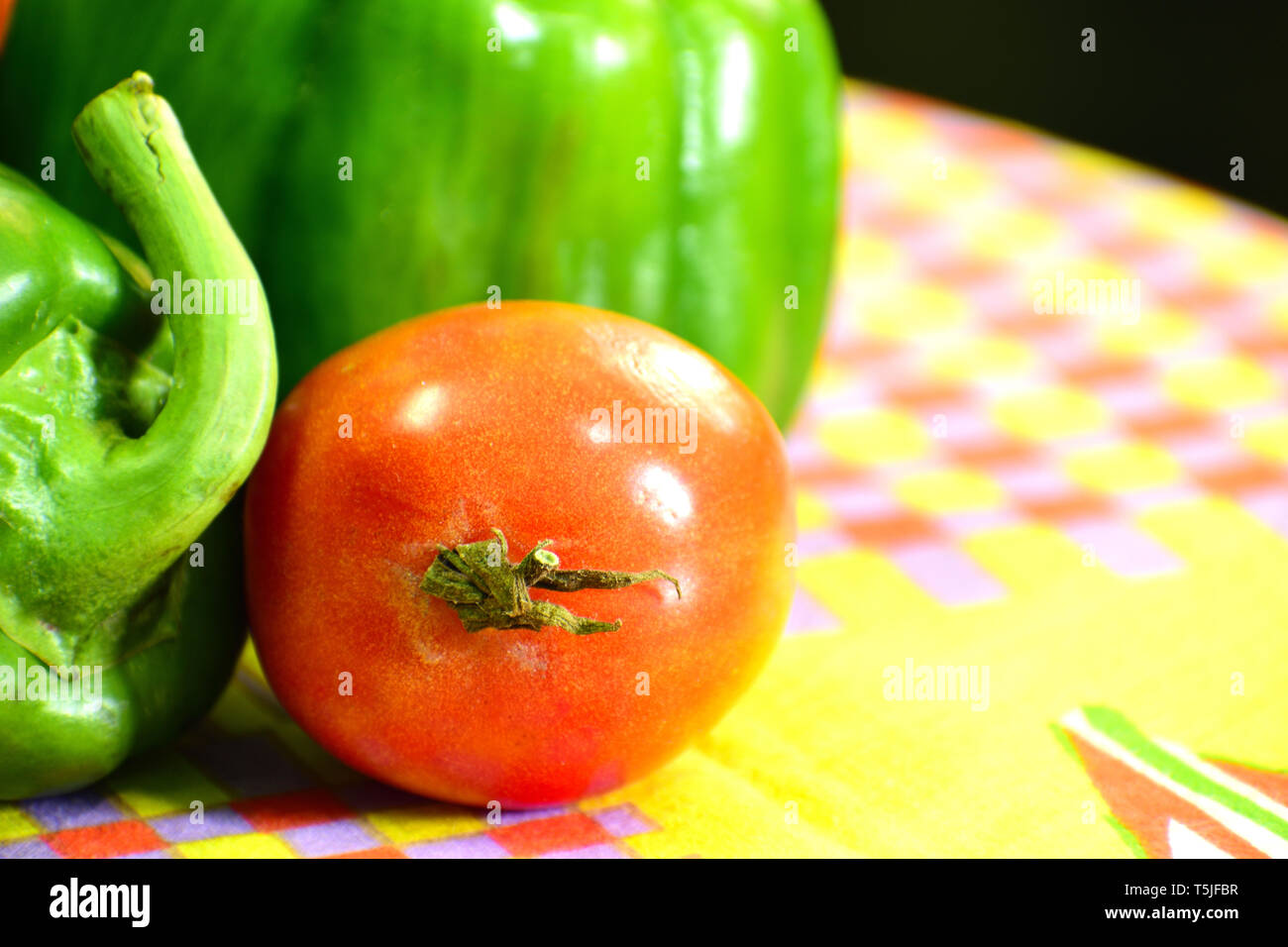 Beau vert capsicum avec une tomate rouge en plan rapproché sur une table Banque D'Images