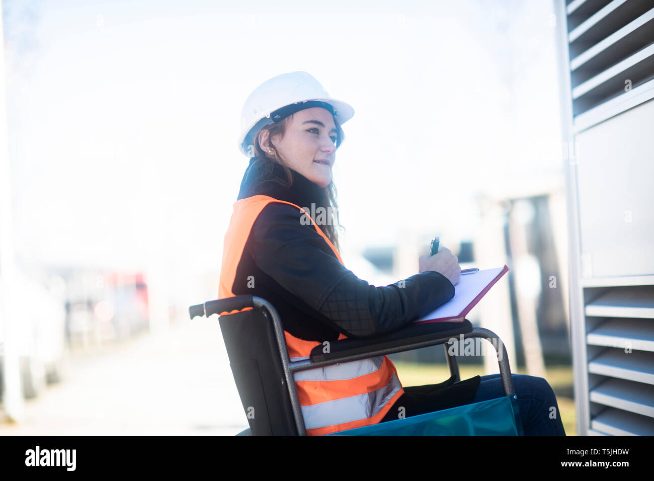 Jeune technicien à casque de sécurité et gilet de travail à l'extérieur en fauteuil roulant Banque D'Images