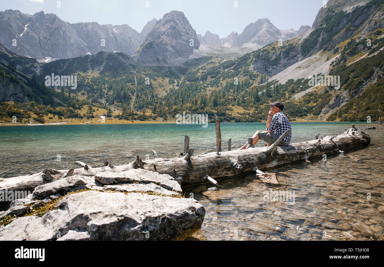 Autriche, Tyrol, man sitting on tree trunk au lac Seebensee Banque D'Images
