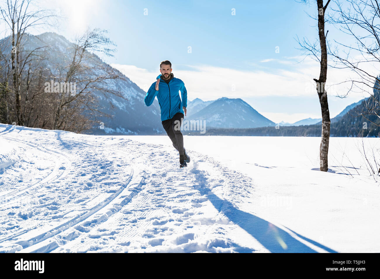 Germany, Bavaria, sportif homme qui court dans la neige en hiver Banque D'Images