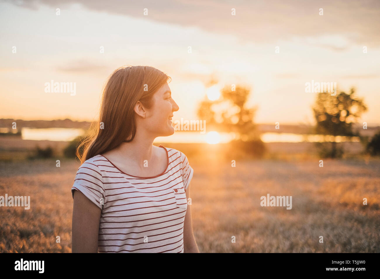 Souriante jeune femme admirant le coucher du soleil dans la nature Banque D'Images