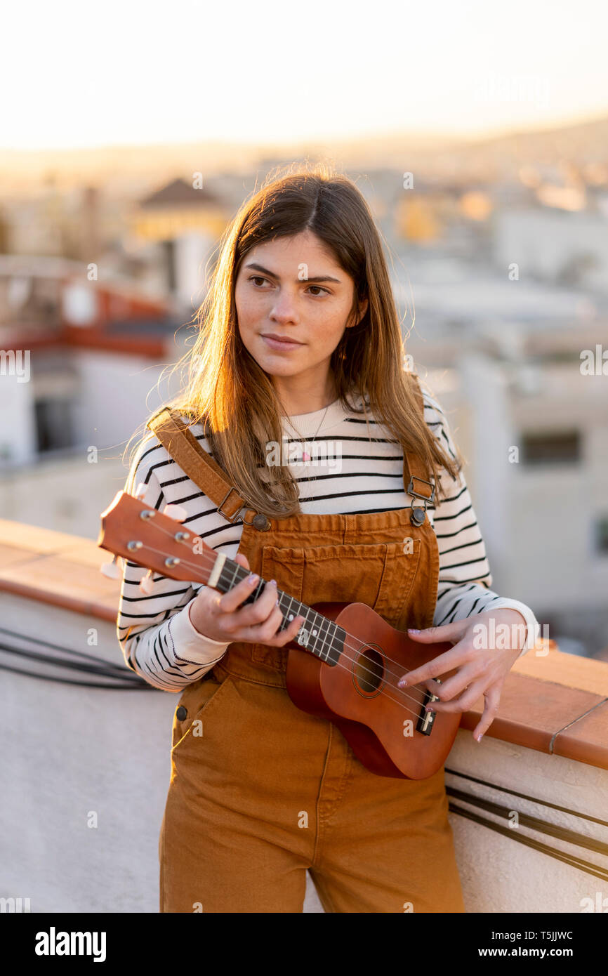 Portrait of young woman standing sur la terrasse du toit dans la soirée à l'Ukulele Banque D'Images