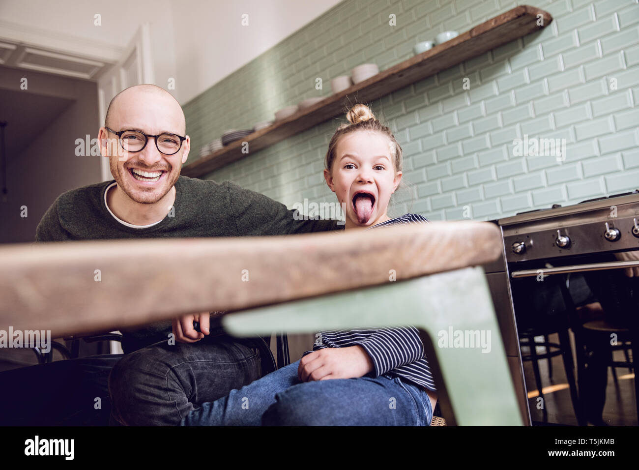 Père et fille assis dans la cuisine, girl pulling funny faces Banque D'Images