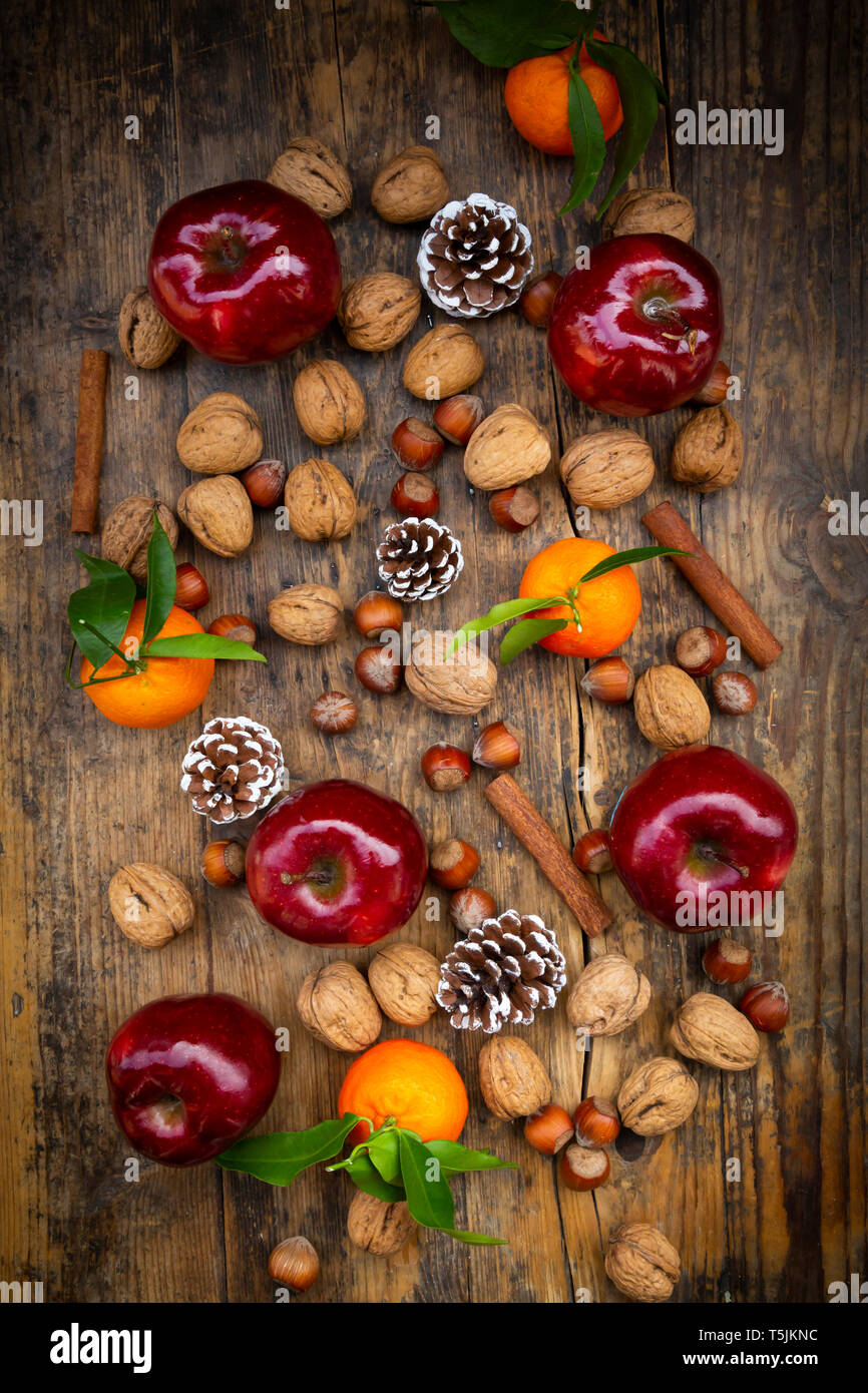 Pommes rouges, tangerines, noisettes, noix, des bâtons de cannelle et des pommes de pin sur le bois foncé Banque D'Images