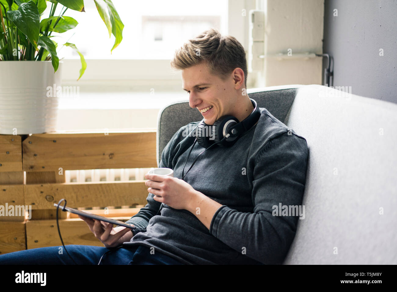 Smiling Young man with tablet et écouteurs sitting on couch Banque D'Images