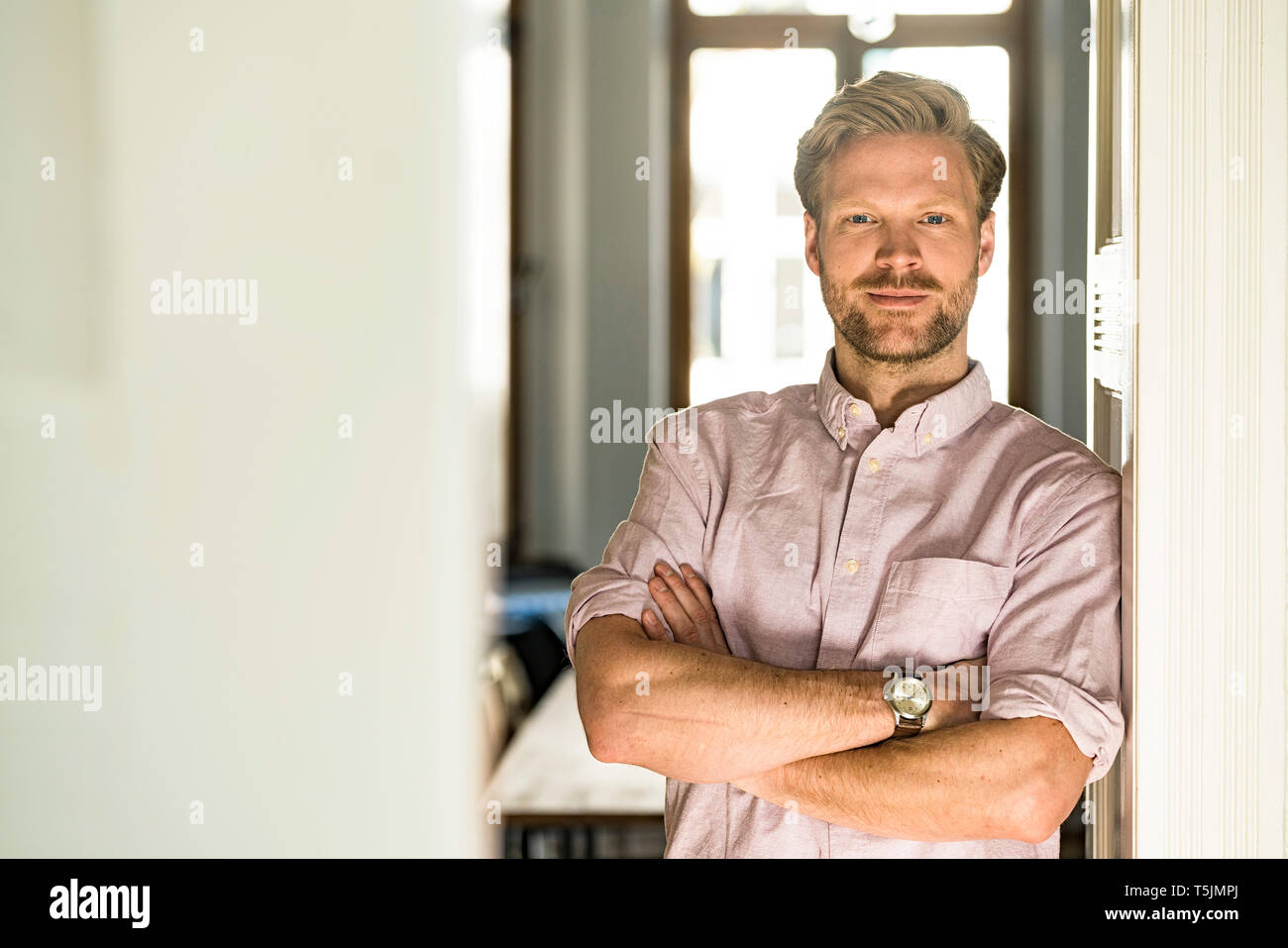 Portrait of smiling casual man leaning against door at home Banque D'Images