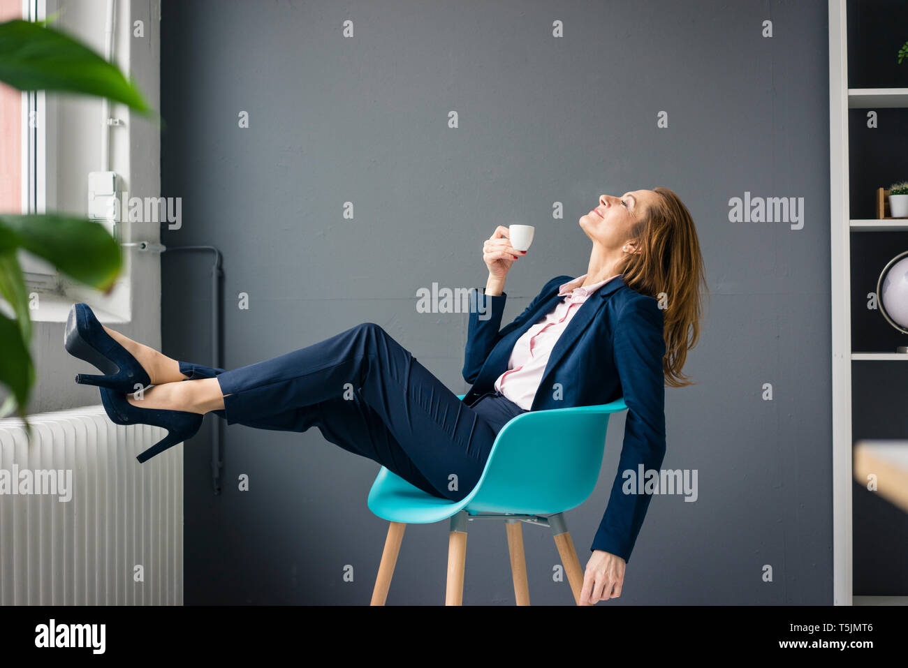 Businesswoman prenant une pause, assis sur une chaise à côté de la fenêtre, de boire du café Banque D'Images