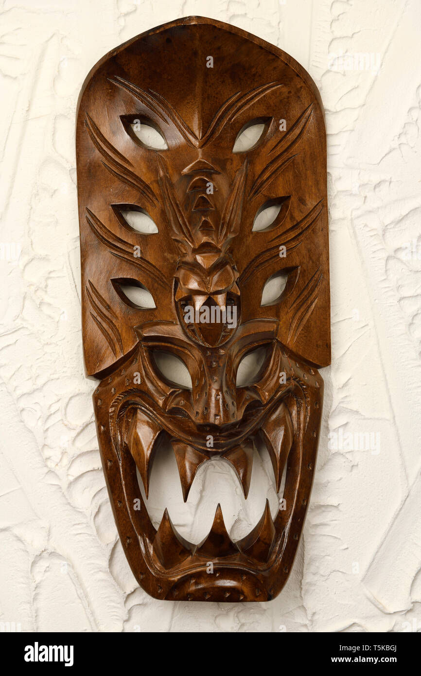 Sculpté en bois masque Tiki Hawaiien de démon aux yeux bleus sur le mur en stuc Banque D'Images