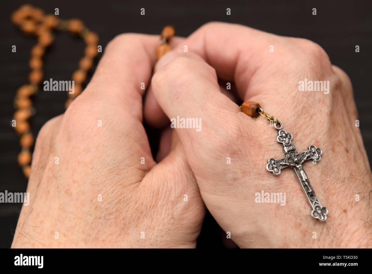 Mains de vieil homme méditant et priant le bois, perles d'un rosaire avec crucifix Banque D'Images
