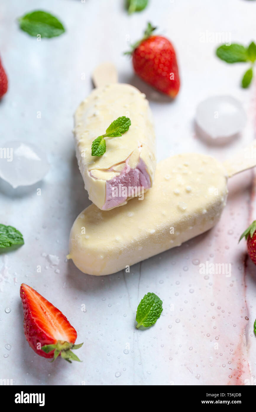 Glace à la fraise sur stick recouvert de chocolat blanc sur la table en marbre, télévision lay Banque D'Images