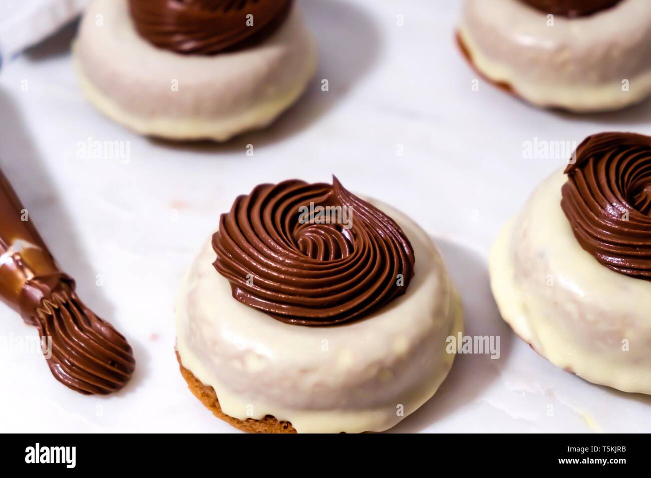 Triple Chocolat Donuts avec Ganache au chocolat crémeux assis sur marbre blanc avec l'extrémité de la tuyauterie sur le côté Banque D'Images