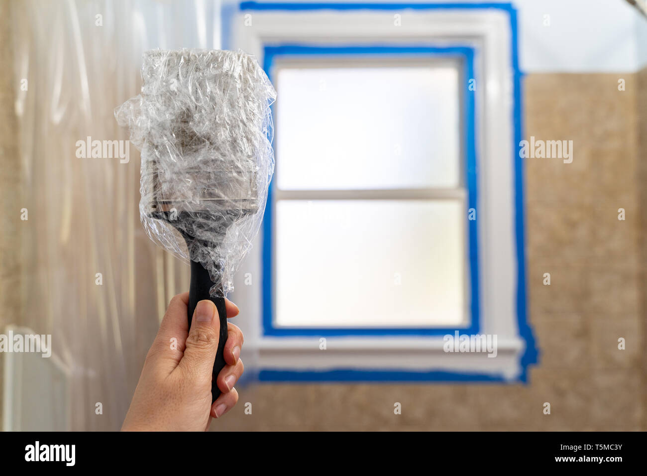 Caucasian woman part contient jusqu'un pinceau enveloppés dans une pellicule de plastique pour protéger le pinceau de sécher pendant que vous attendez d'une nouvelle couche de peinture Banque D'Images