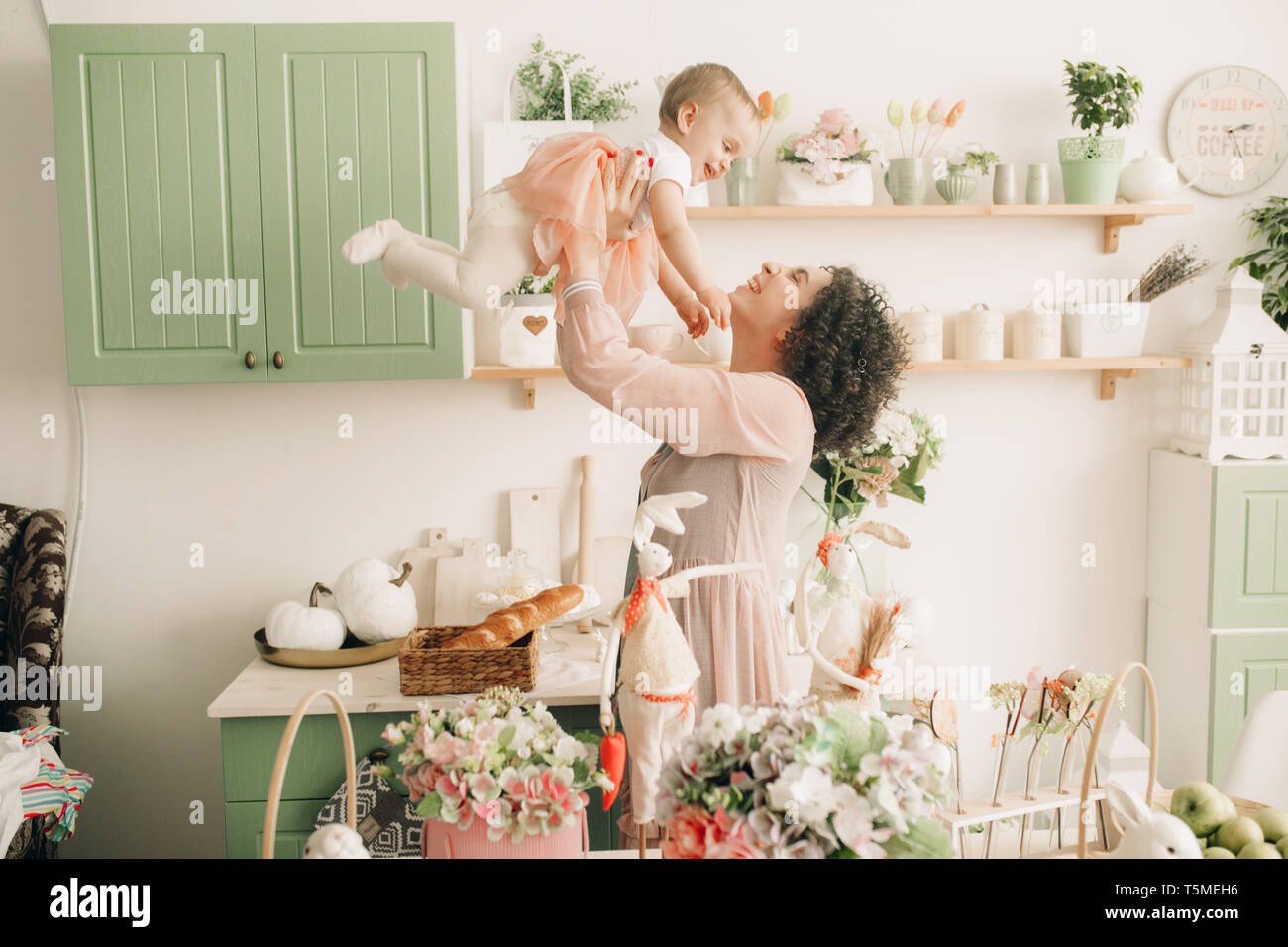 Heureuse mère joue avec son bébé dans la cuisine sur fond de décorations de Pâques. Banque D'Images