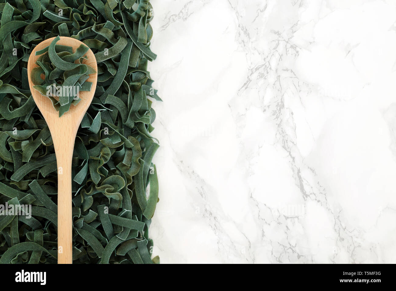 Tagliatelles à la spiruline pâtes alimentaires de santé sur une cuillère à olive en vrac et formant un motif de fond sur du marbre. Riche en protéines et fibres. Banque D'Images