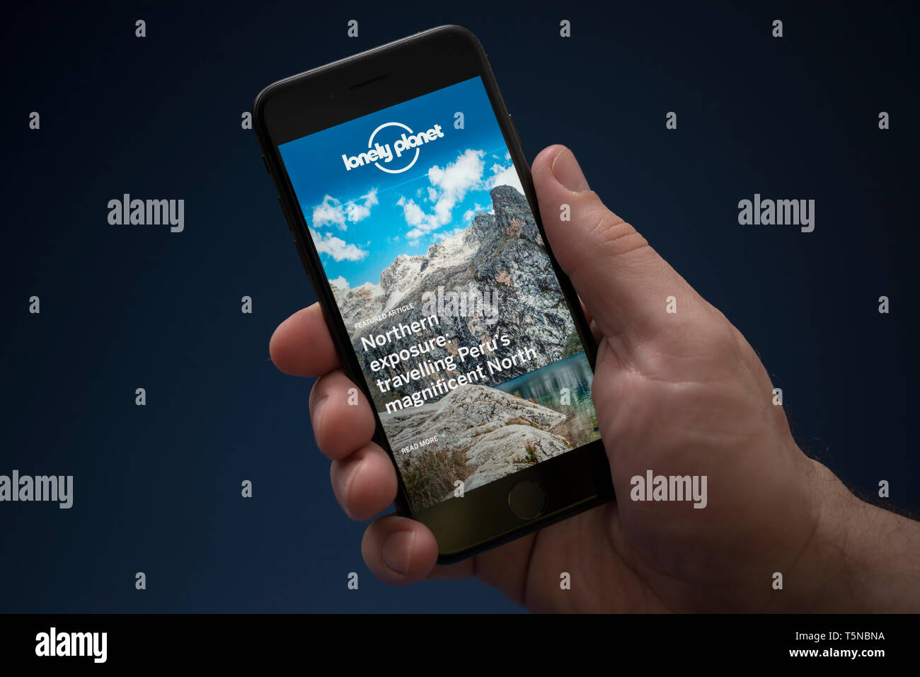 Un homme se penche sur son iPhone qui affiche le logo Lonely Planet (usage éditorial uniquement). Banque D'Images