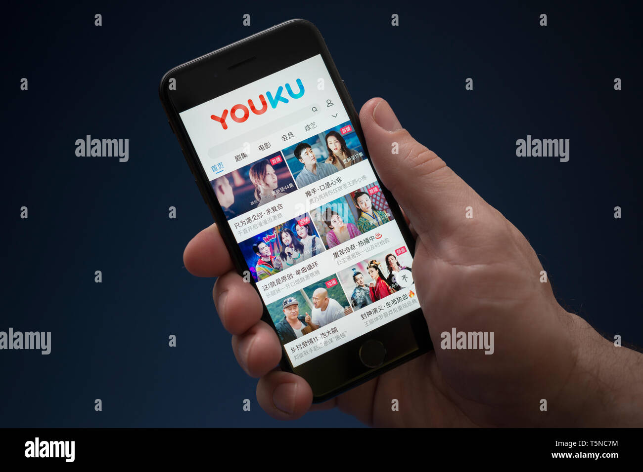Un homme se penche sur son iPhone qui affiche le logo Youku (usage éditorial uniquement). Banque D'Images