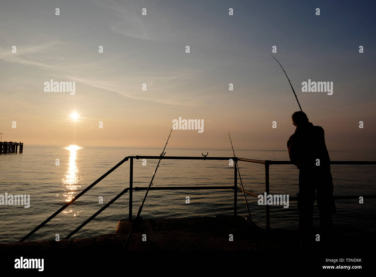 La pêche à la ligne d'accouplement à l'aide de pêcheurs beach dominante de la passerelle au-dessus de Totland Bay alors que le soleil se couche sur l'horizon lointain et Totland Pier. Banque D'Images