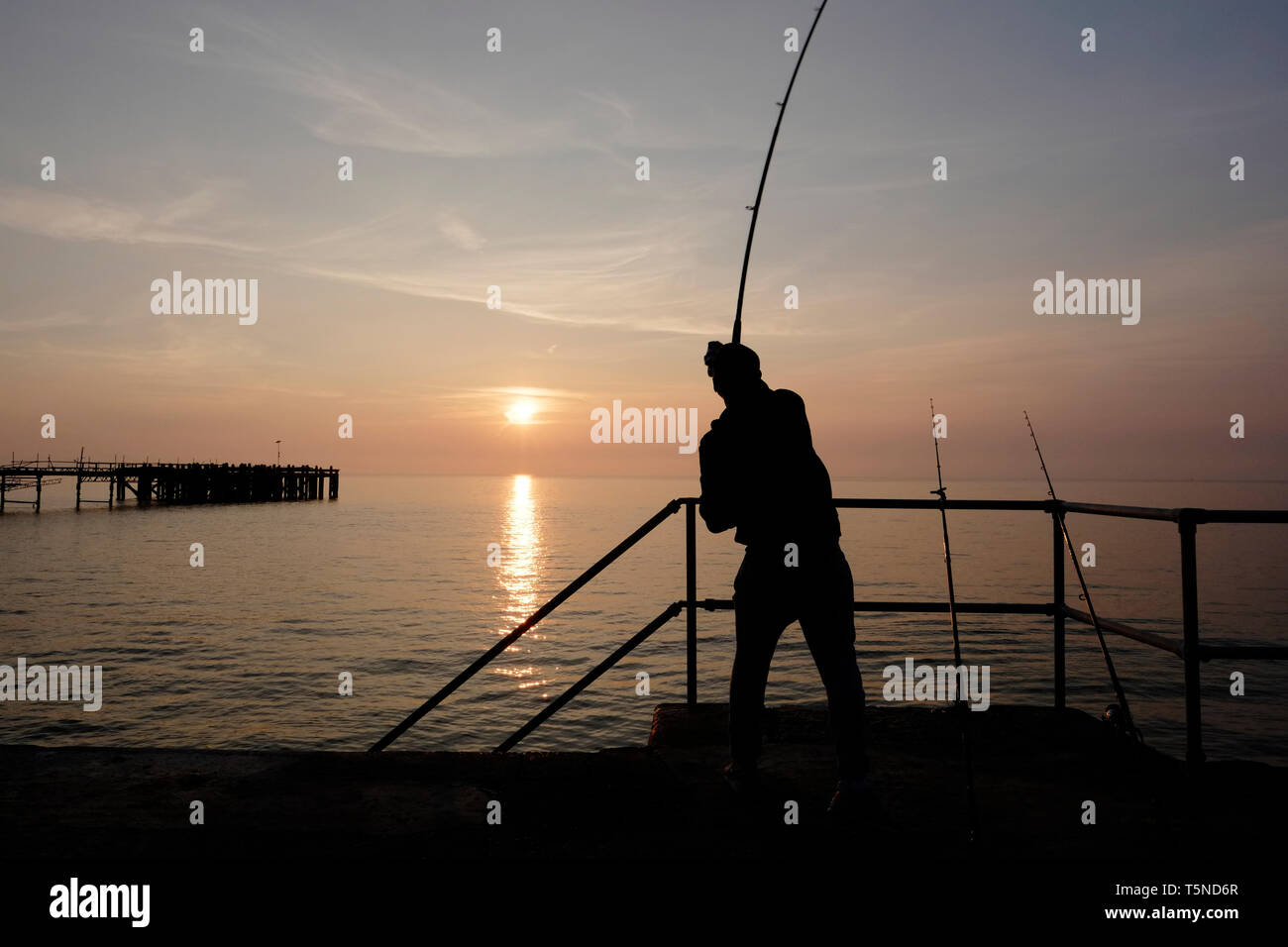 La pêche à la ligne d'accouplement à l'aide de pêcheurs beach dominante de la passerelle au-dessus de Totland Bay alors que le soleil se couche sur l'horizon lointain et Totland Pier. Banque D'Images