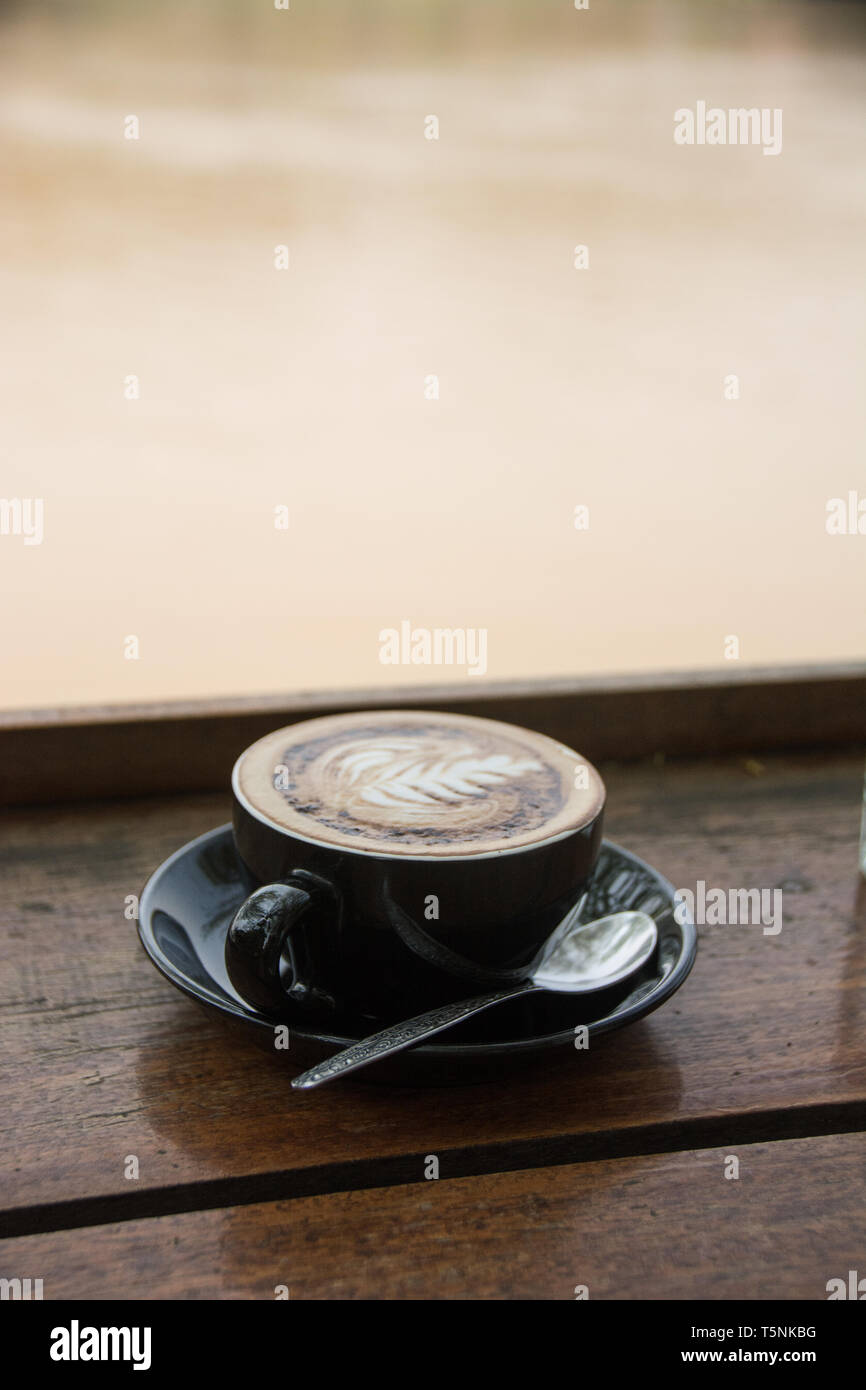 Un cappuccino magnifique dans une tasse noire surplombant le Mékong à Luang Prabang, au Laos. Banque D'Images