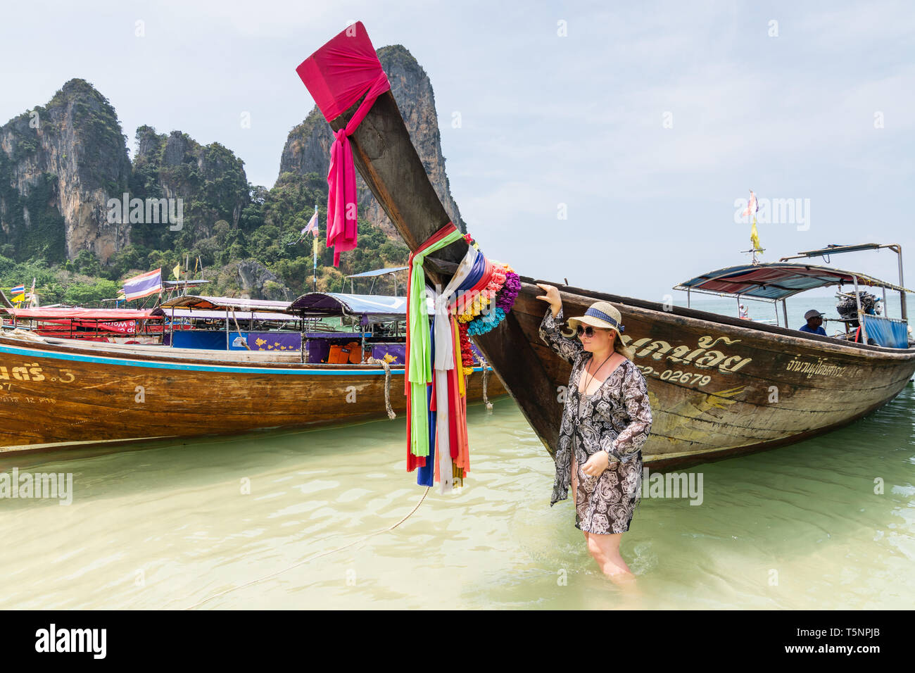 KRABI, THAÏLANDE - Mars 2019 : femme se trouve à côté de la longue queue des bateaux amarrés à Railey beach. Banque D'Images