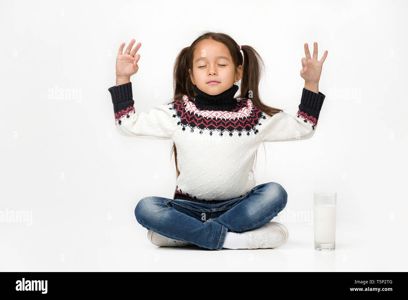 Portrait of cute petit enfant fille assise en position du lotus et un verre de lait frais est à proximité Banque D'Images
