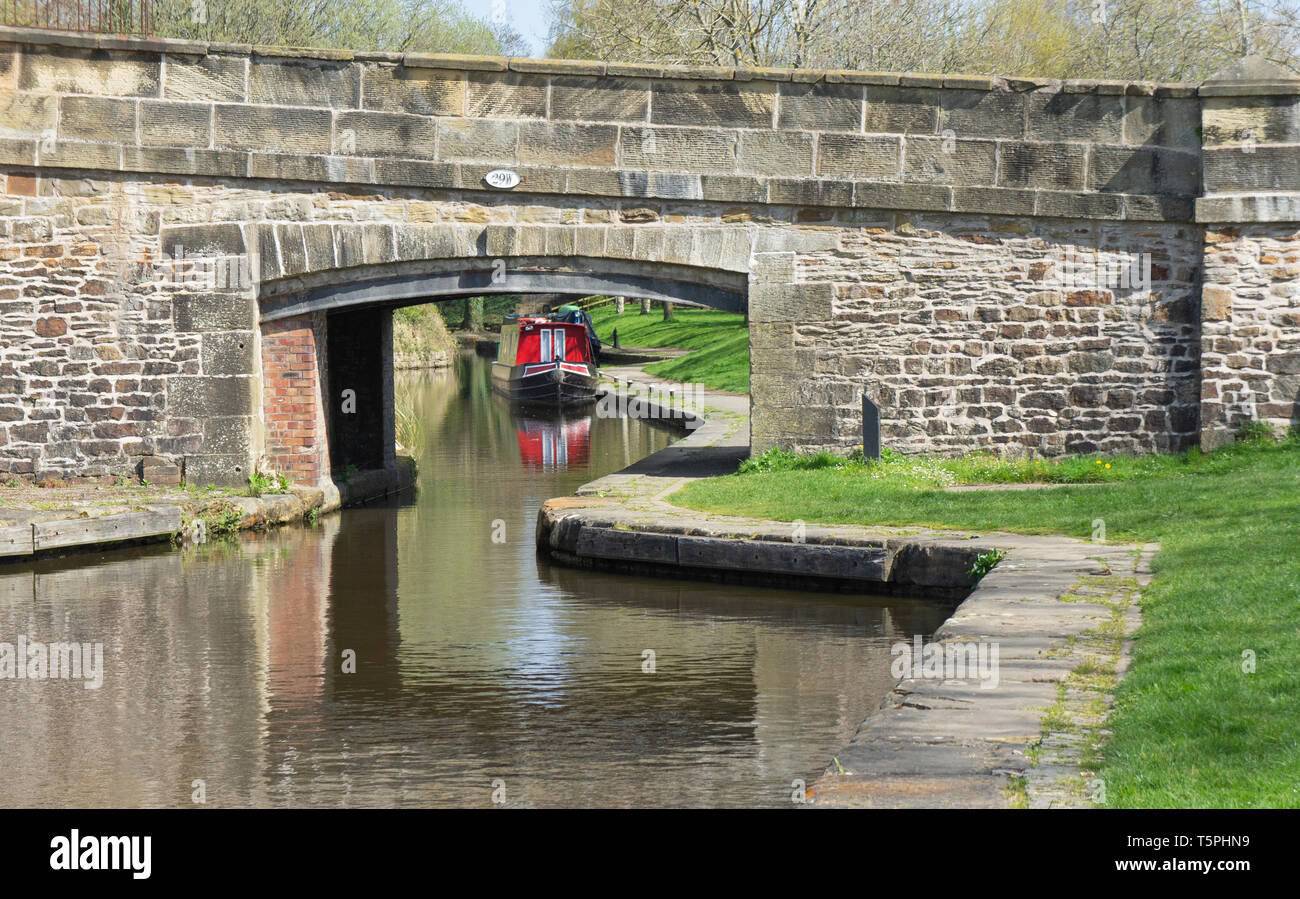 Une vue sur un canal et sous un vieux pont de pierre, à quai de Llangollen, Pays de Galles, avec un grand classique rouge amarré de l'autre côté avec l'ensemble des reflecti Banque D'Images