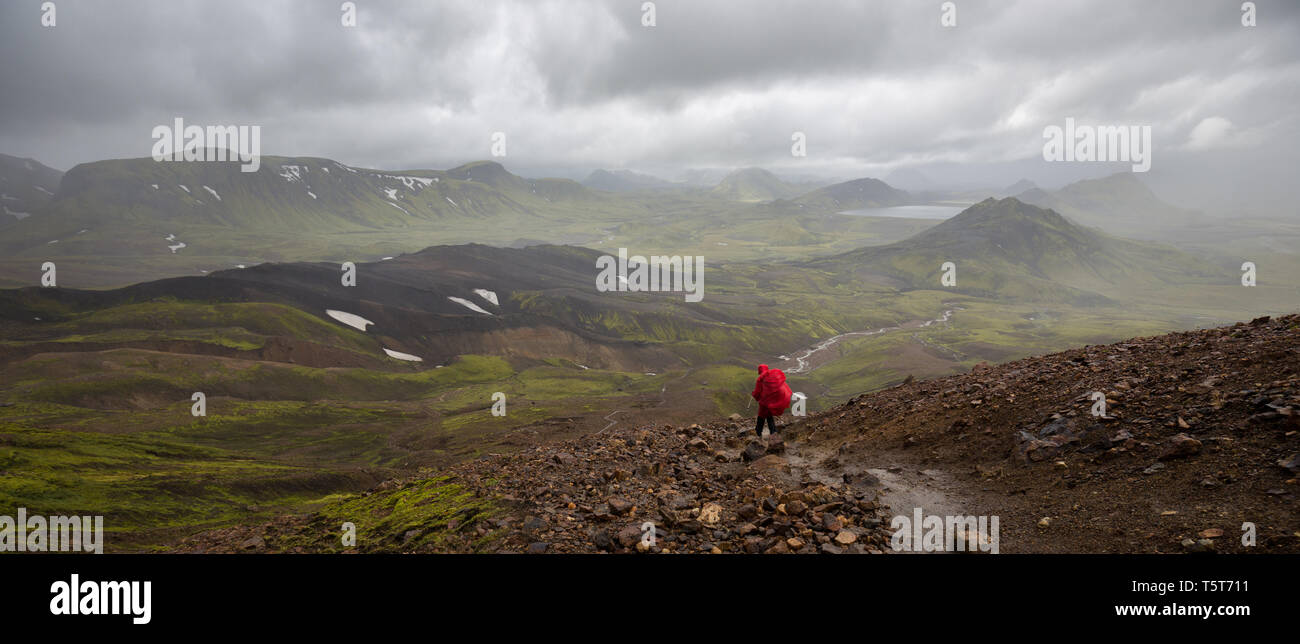 Une personne dans une cape de pluie rouge le sentier de randonnée Laugavegur en Islande avec une vue à couper le souffle dans une vallée. Banque D'Images