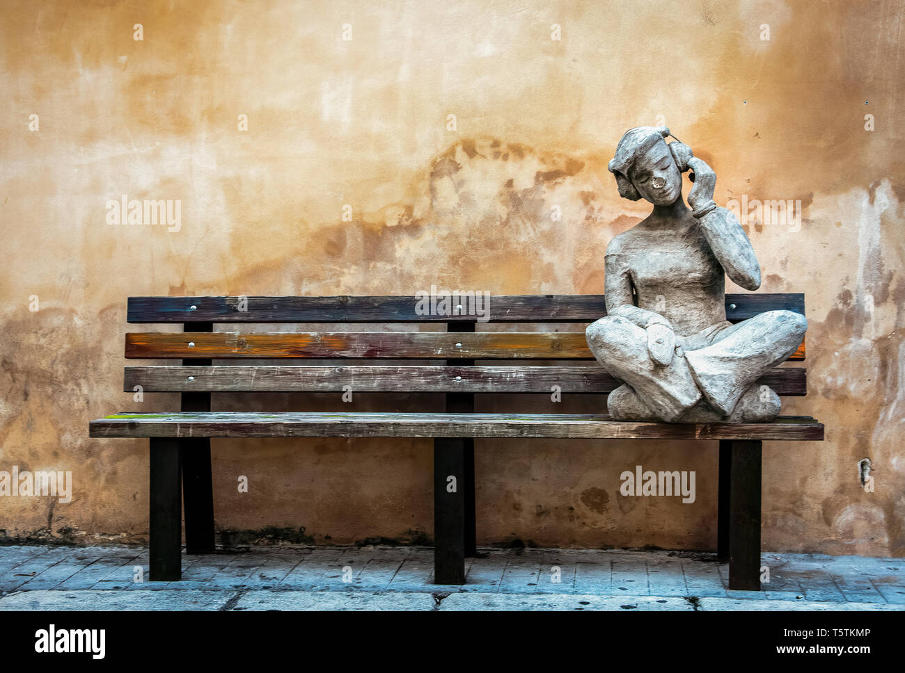 Statue de pierre d'un jeune homme assis et écouter de la musique sur un banc en bois Banque D'Images