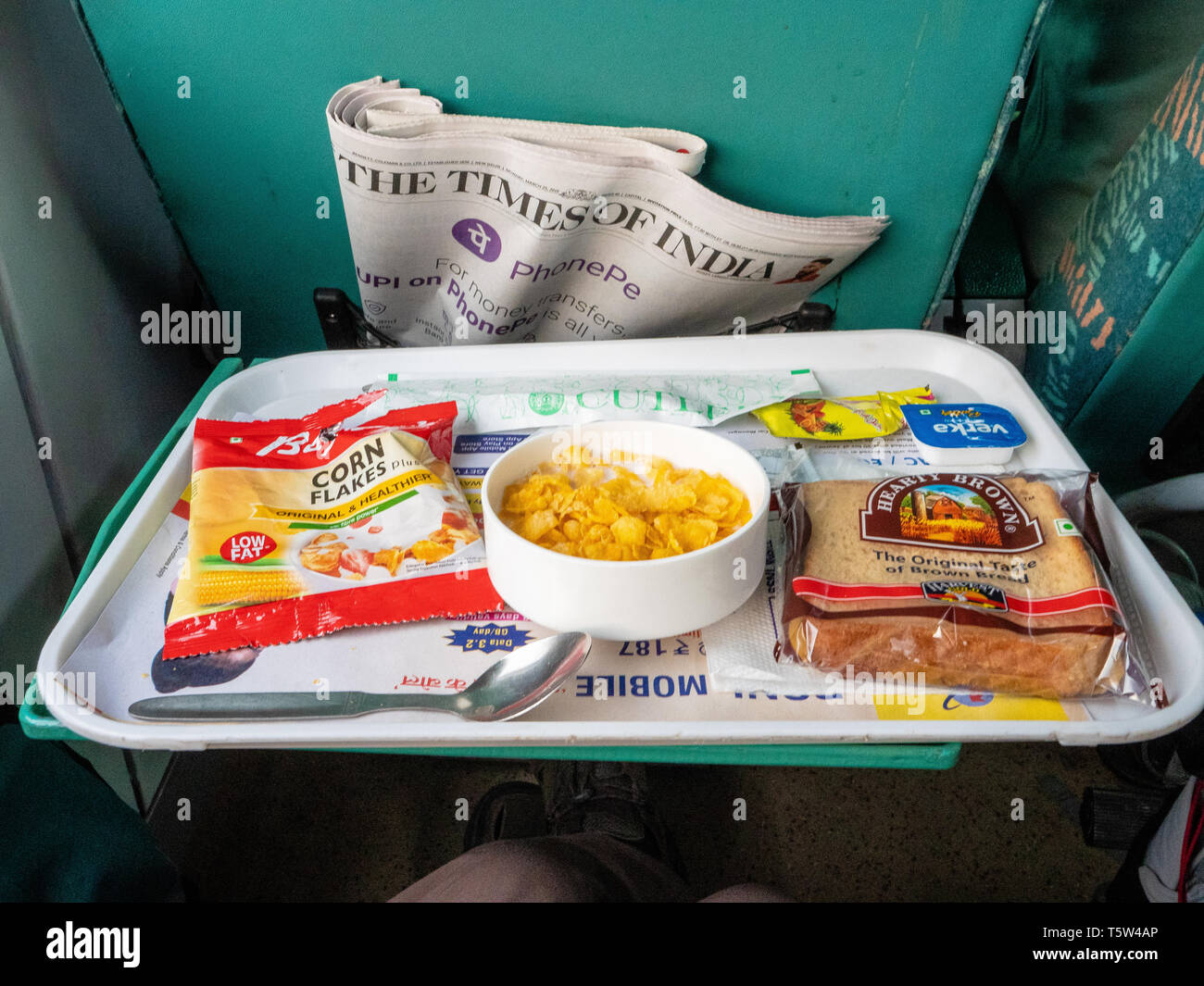 Siège de première classe sur les chemins de fer indiens express avec une copie de l'Indian Times et petit déjeuner avec des flocons de maïs grillé et empaqueté Banque D'Images