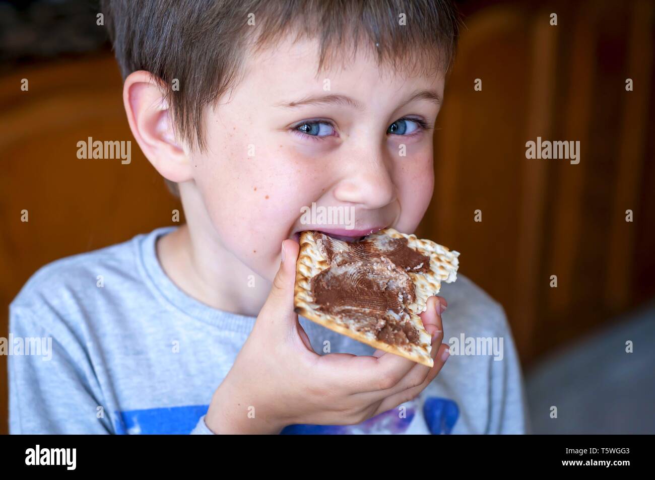 Un closeup portrait of a cute blue-eyed enfant mangeant un cracker matzoh avec pâte à tartiner au chocolat. Banque D'Images