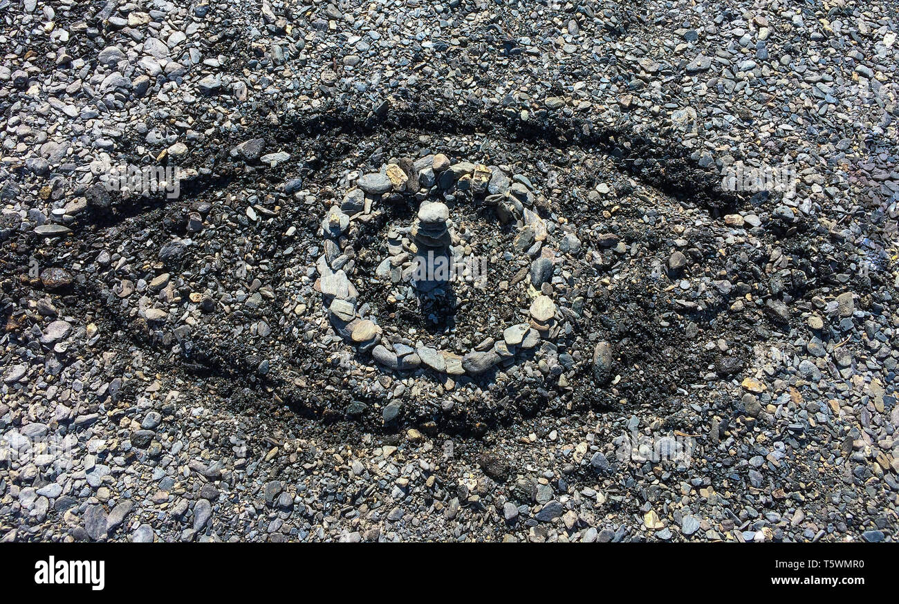 L'œil symbolique faite de pierres et de sable sculpté sur une plage de galets de l'été - Concept de big brother, omniprésence de Dieu ou la surveillance publique. Banque D'Images