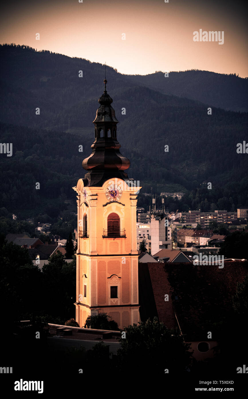 Vieux clocher de l'église avec une horloge en face d'une ville autrichienne au coucher du soleil Banque D'Images
